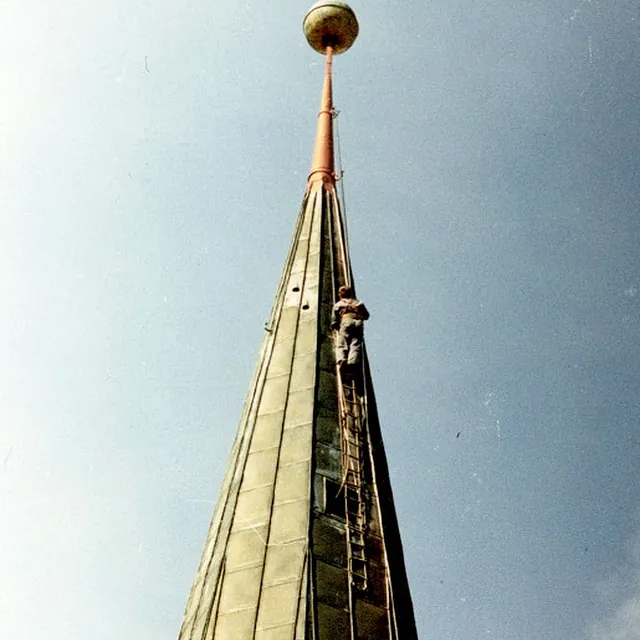 Arbeiter auf der Kirchturmspitze bei blauem Himmel.