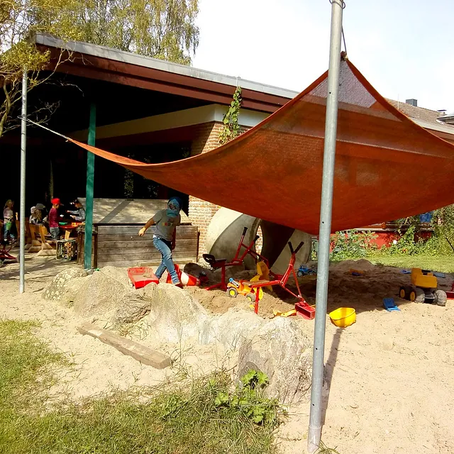 Kinder spielen im Sand unter Sonnenschutz